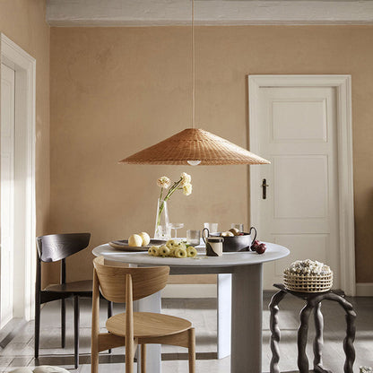 A cluster of three conical rattan pendant lights in varying tall funnel and flat sun hat shapes hanging above a light wood dining table.