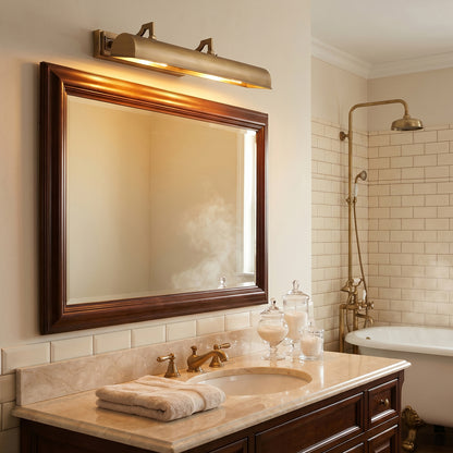 A classic bathroom vanity setup featuring a large rectangular mirror with a dark wood frame, a warm brass wall sconce above, a marble countertop with an integrated sink, and a white bathtub in the background.
