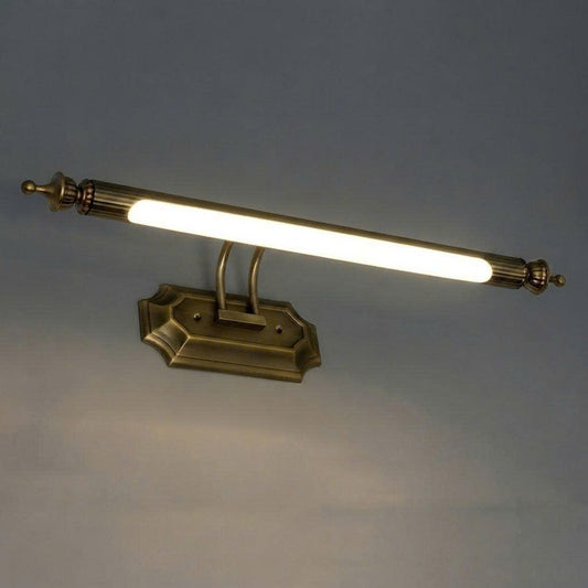 A classic wall-mounted light fixture with an antique brass finish and a glowing white tube bulb, set against a plain gray wall.