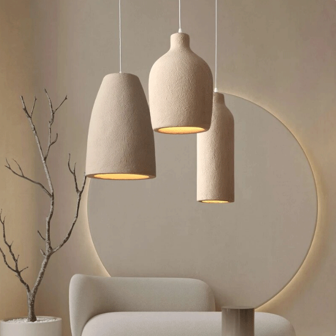 Three minimalist beige ceramic pendant lights hanging in a Japandi style living room with a round mirror.