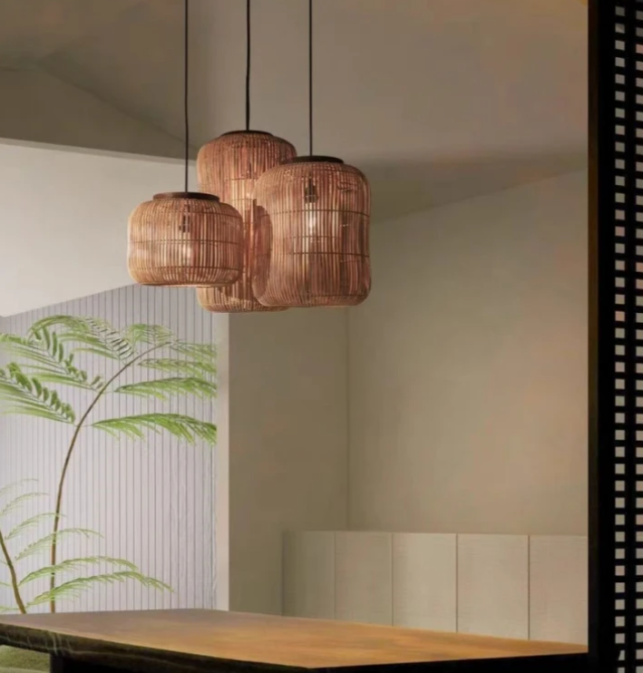 A cluster of three natural rattan lantern lights with fine vertical slats, hanging at staggered heights over a dark wooden window shutter background.