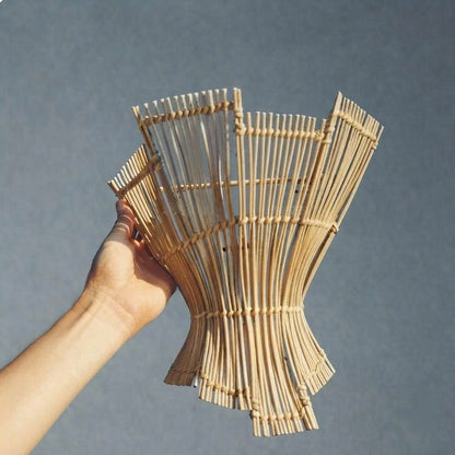 A hand holding a handmade woven bamboo or rattan planter vase against a solid gray background.