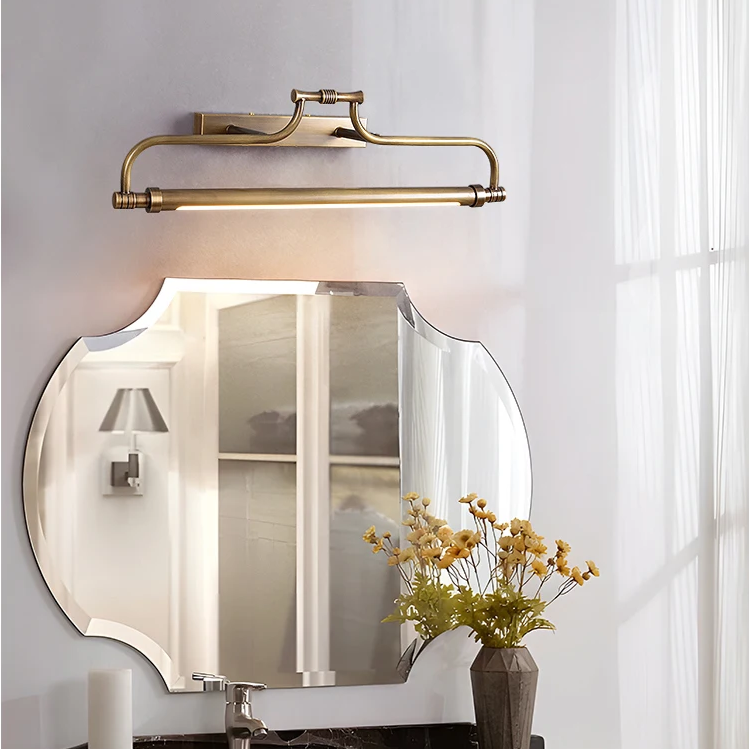 A wall-mounted brass bathroom light fixture with a curved horizontal bar and integrated light, shown above a decorative mirror in a bright bathroom setting.