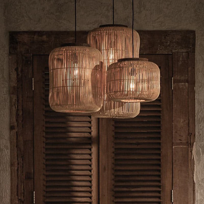 Three staggered Japandi cylinder wicker pendant lamps emitting a warm amber glow in a moody interior setup.