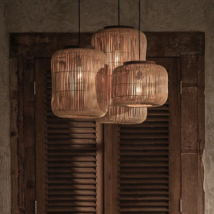 Three staggered Japandi cylinder wicker pendant lamps emitting a warm amber glow in a moody interior setup.