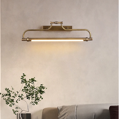 A wall-mounted linear light fixture with a warm brass finish and a glowing horizontal bar, shown installed on a beige wall above a sofa with a small plant in the foreground.