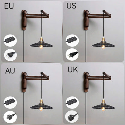 Four-panel comparison of a wall-mounted pendant light shown from different side angles, labeled EU, US, AU, and UK. The fixture has a dark brown angled wall bracket, a black scalloped metal shade, a warm glowing bulb, and inset circles showing the power switch and plug for each region.
