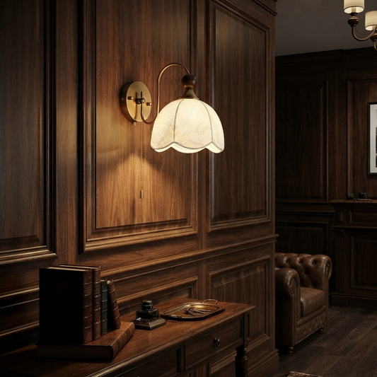 A vintage-style wall sconce with a warm glowing white bell-shaped glass shade and an antique brass fixture, mounted on a dark wood paneled wall in a classic room setting.