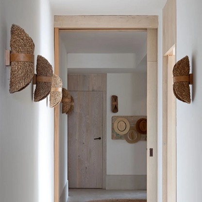 A set of four woven seagrass wall sconces with brown leather straps, mounted symmetrically on the white walls of a minimalist hallway with light wood doorframes.