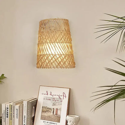 Woven rattan wall light fixture on a neutral wall with books and a plant.