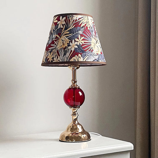 Decorative table lamp with a floral-patterned shade and red glass base on a white surface.