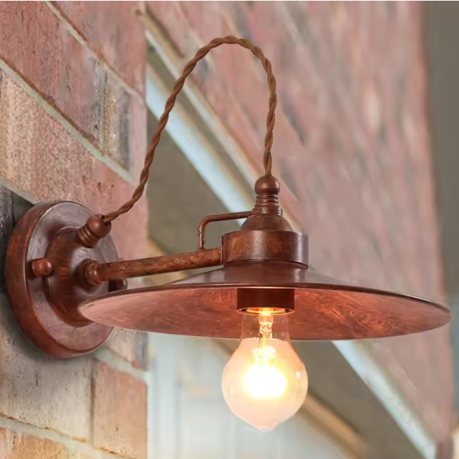 Rustic wall-mounted light fixture with a wide metal shade, twisted hanging cord, and glowing bulb, shown mounted on a brick wall.