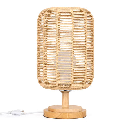 A natural rattan table lamp with a cylindrical woven shade and a round wooden base, shown on a white background with its power cord visible.