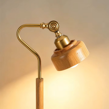 A modern adjustable floor lamp with a warm brass metal arm and a round light-wood shade, shown illuminated against a soft beige background.