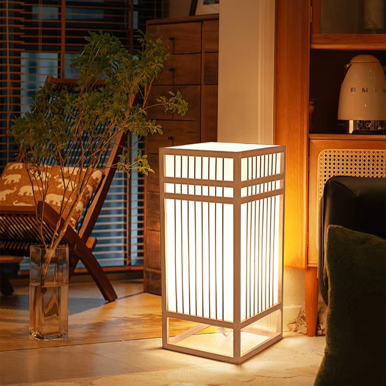 A modern Japanese-style rectangular floor lamp with a white illuminated slatted screen and a light wood frame, placed on a tiled floor in a cozy, warmly lit living room.