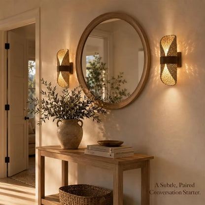 Round mirror on a wall with two wall sconces and a wooden console table with decor items.