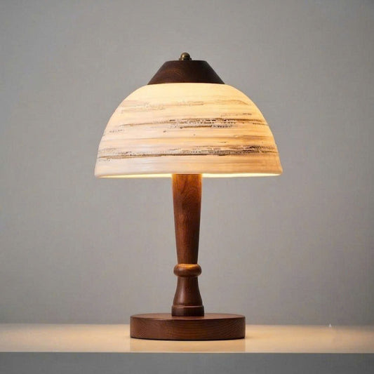 A table lamp with a warm glowing shade featuring horizontal beige and brown wood grain patterns, supported by a dark brown wooden stem and base, set against a neutral gray background.