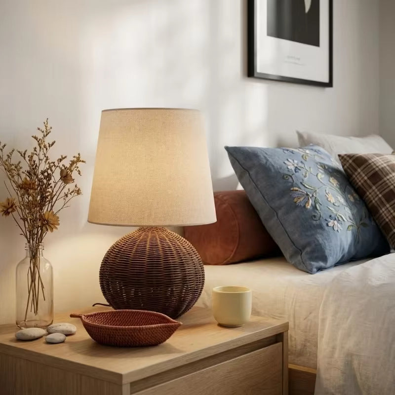 Nighstand with lamp, decorative items, and pillows on a bed in a bedroom setting.