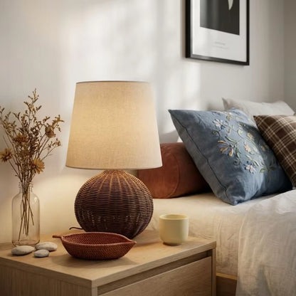 Nighstand with lamp, decorative items, and pillows on a bed in a bedroom setting.
