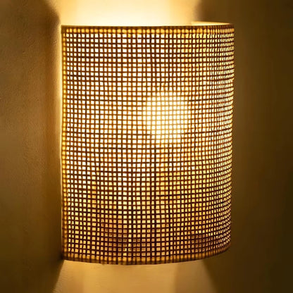 A cylindrical wall sconce with a warm glowing mesh shade, mounted on a textured beige wall.